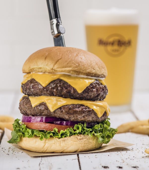 Double decker cheeseburger from Hard Rock Cafe with a glass of beer behind it.